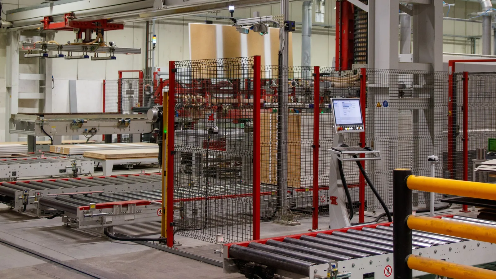 Cellule de palettisation automatisée sous portique, protégée par des grillages rouges, dans un hall industriel