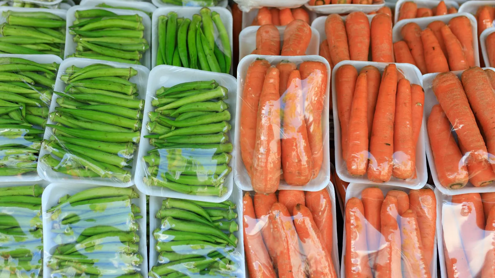 Barquettes thermoformées garnies de gombos et de carottes sous film sur un étal