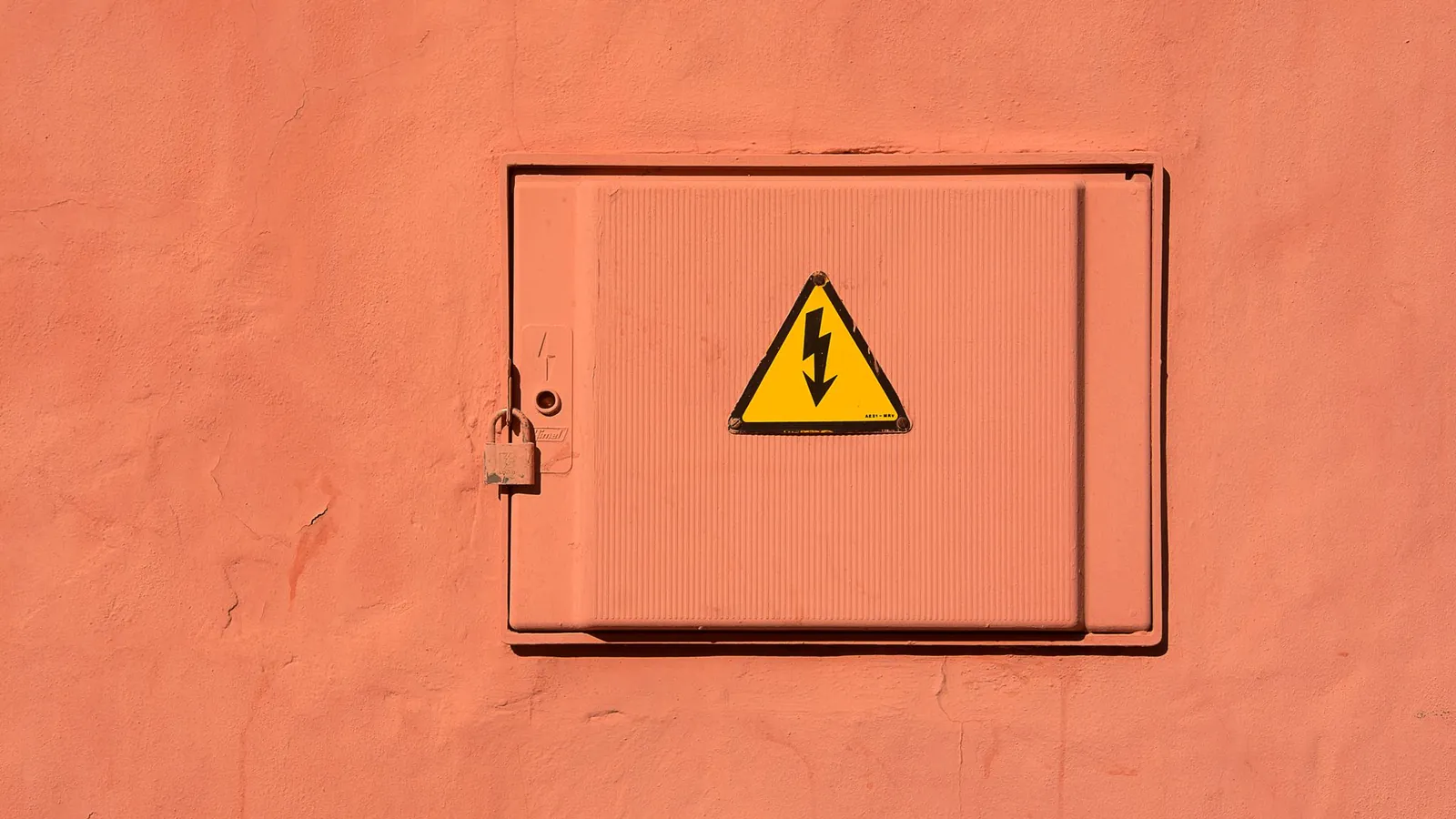 Porte de coffret en tôle pliée encastrée dans un mur, cadenas et pictogramme de danger électrique